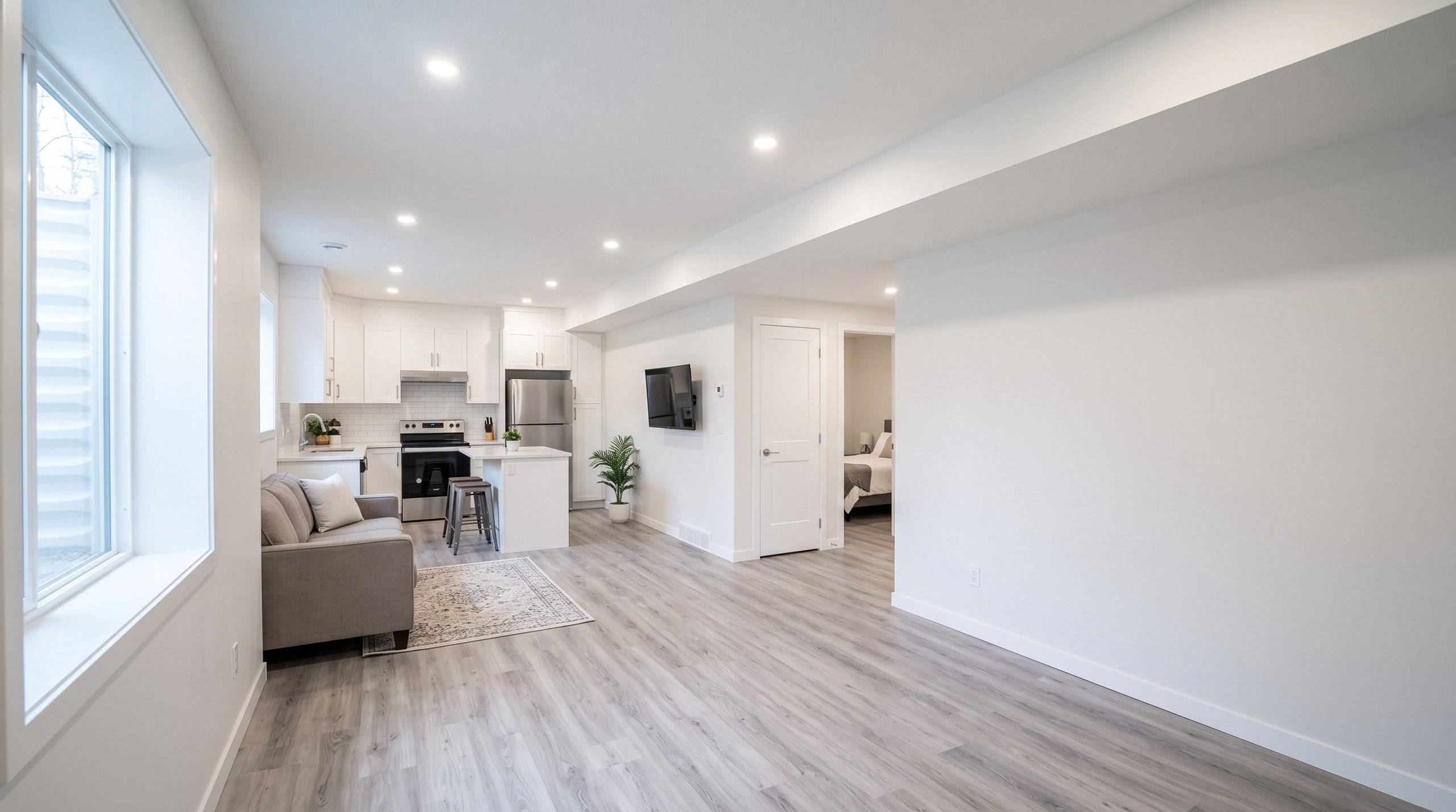 A bright, finished basement suite with an open kitchen, living area and bedroom